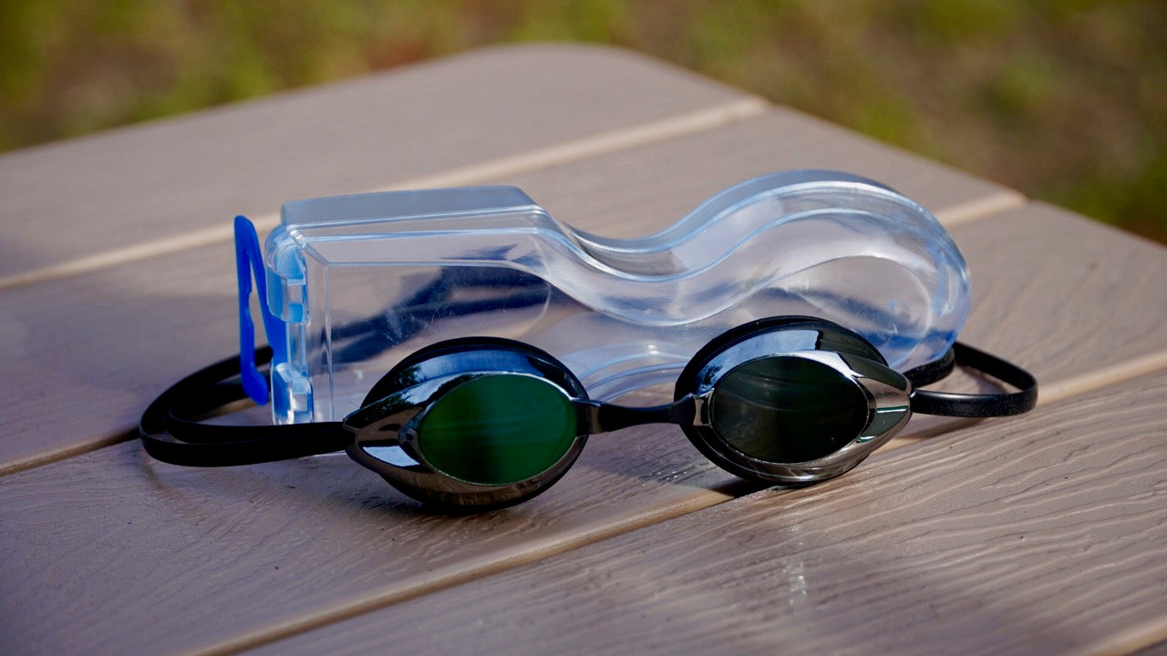 Mirrored smoke/mirror swim goggles with hard clamshell case on wooden pool deck